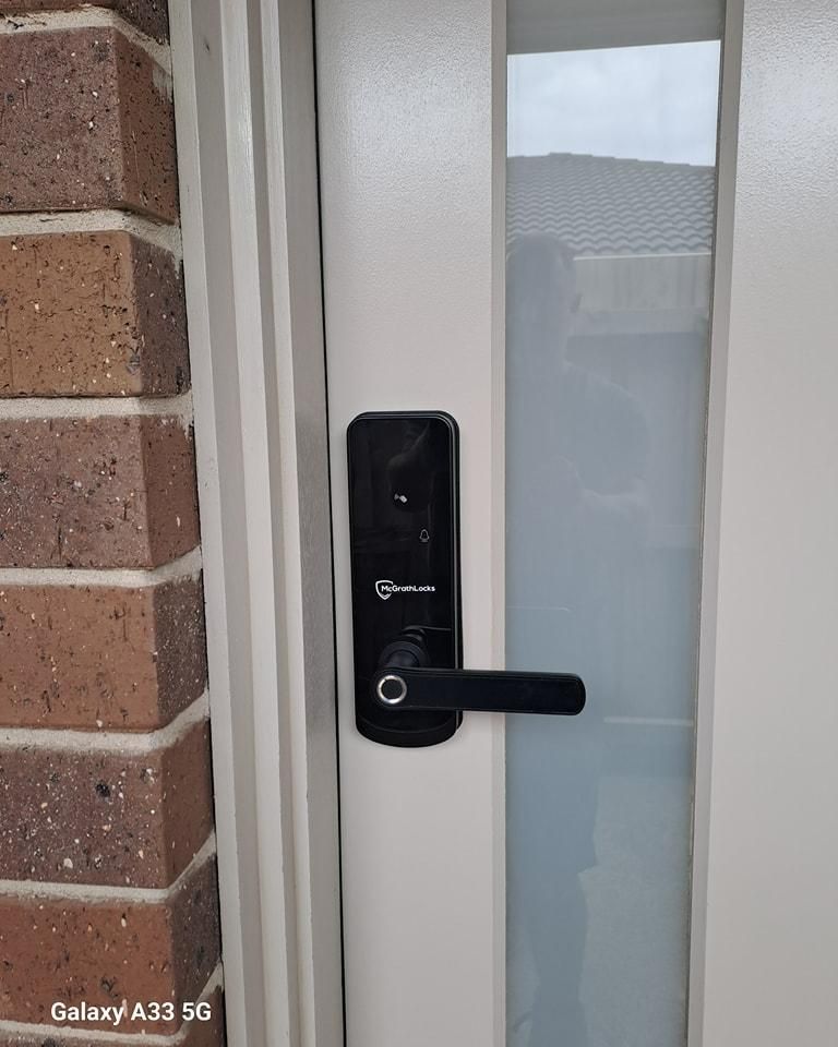 A Smart Door Lock Is Installed on A White Door Next to A Brick Wall — New Lock & Safe Services in Terang, VIC