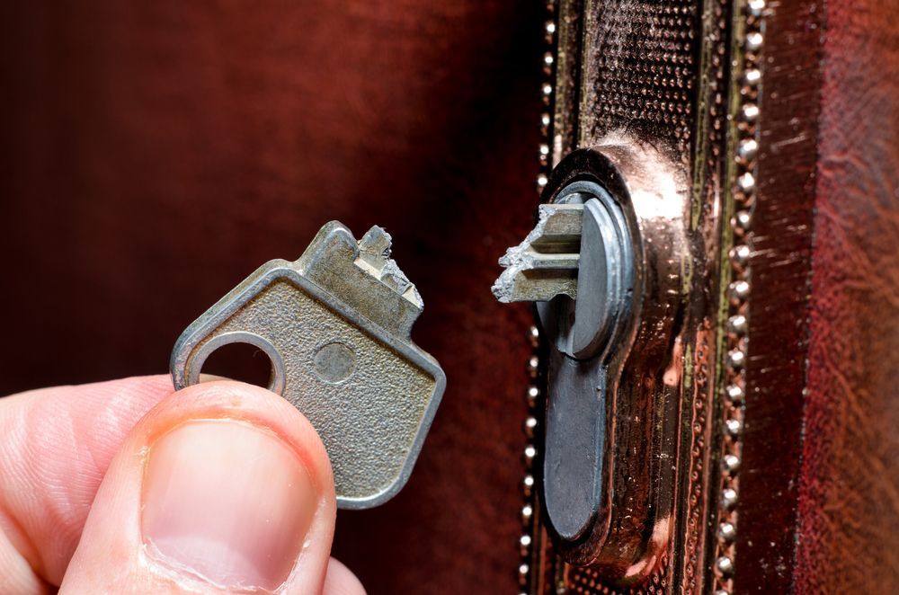 A Person Is Holding A Broken Key In Front Of A Door Lock — New Lock & Safe Services in Camperdown, VIC
