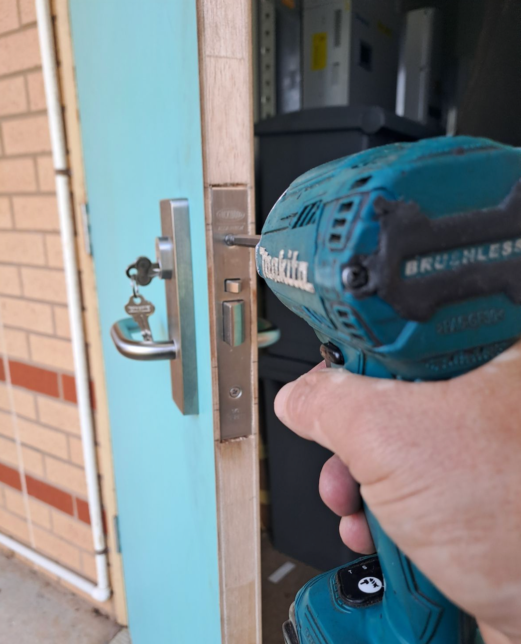 A Man Is Using A Drill To Fix A Door Lock — New Lock & Safe Services in Terang, VIC