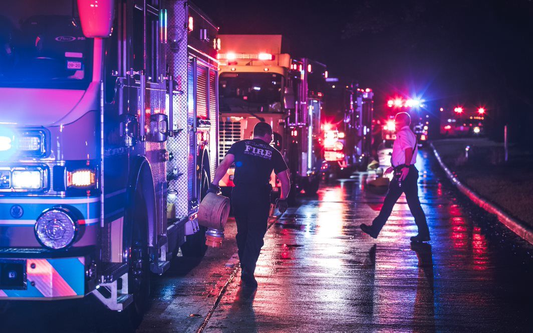 A firefighter is walking towards a fire truck at night.