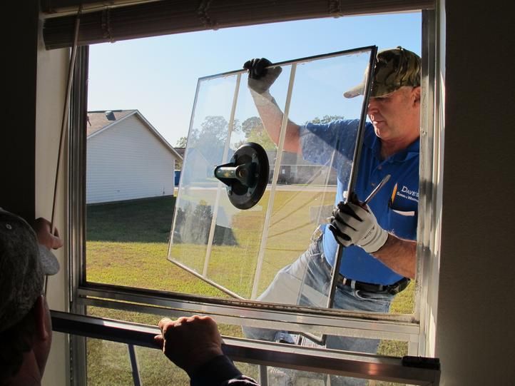 Two workers wearing gloves carefully handling a large sheet of glass in a factory setting.