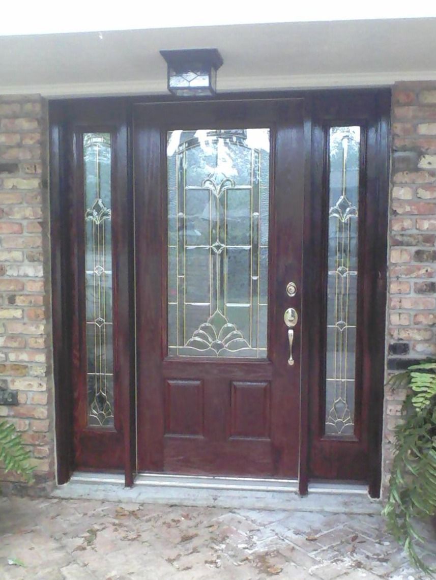 Man on a ladder taping plastic to a glass sliding door, preparing to paint a wall outdoors.