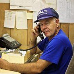 Man in blue shirt and cap on phone at desk with papers, rotary phone, and clipboard.
