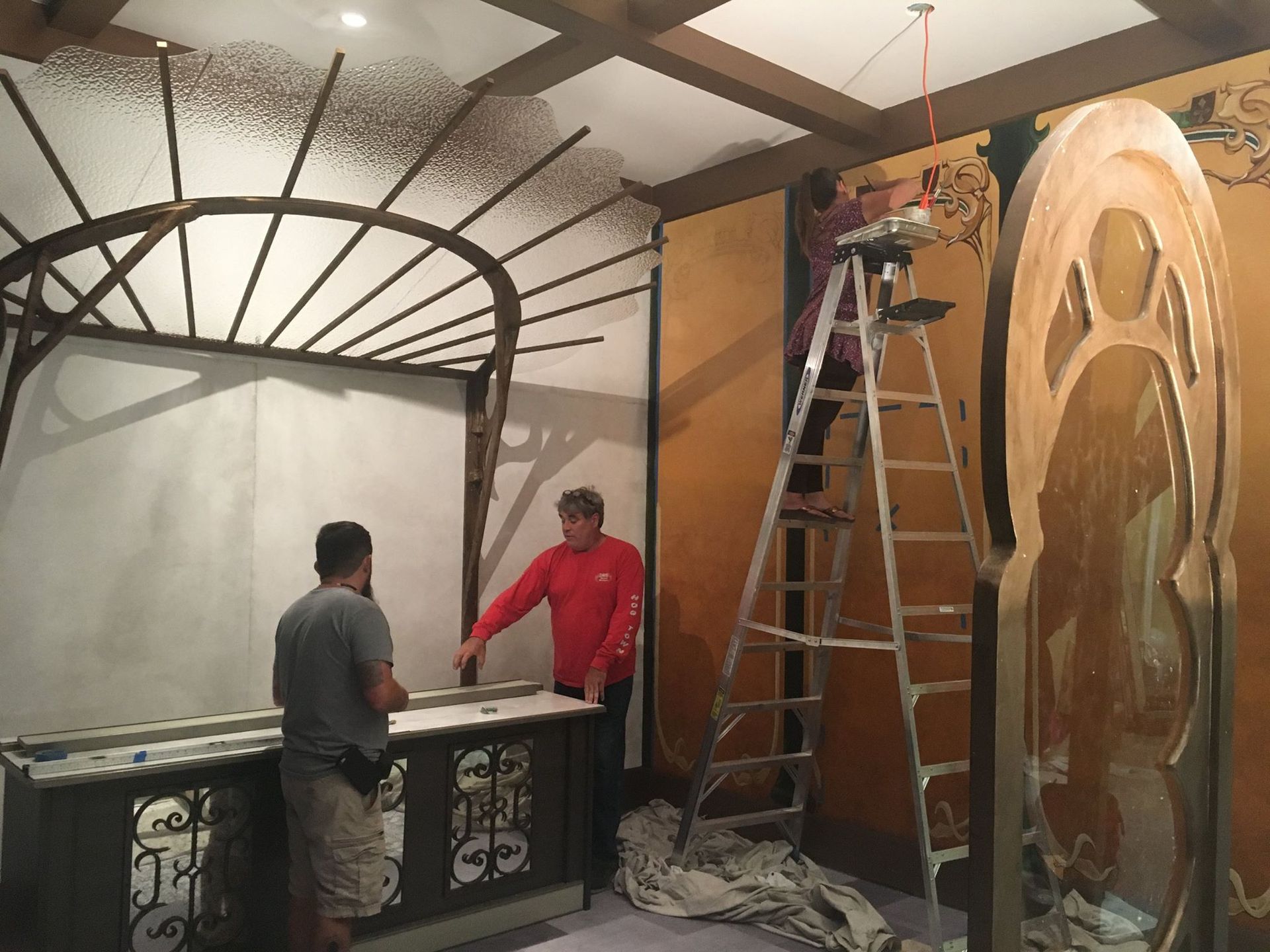 Men installing ornate architectural elements in a room with a gold and beige color scheme.
