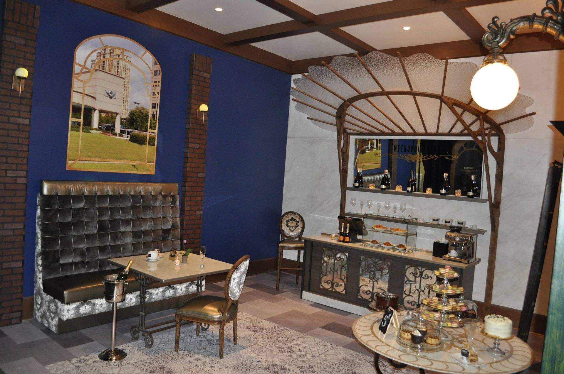 Elegant cafe interior with a velvet booth, bar, and ornate details. Blue walls, brick, and warm lighting.