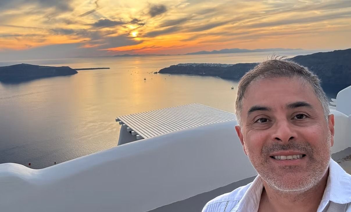 Man smiles for selfie with sunset over the sea in Santorini, Greece.
