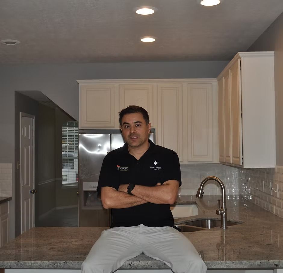 Man sitting on a kitchen counter with arms crossed. White cabinets, stainless steel appliances in a neutral-toned kitchen.
