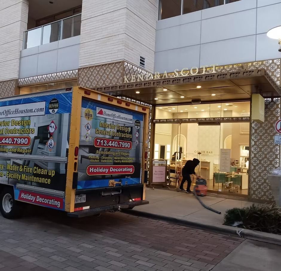 Truck outside a building, a person vacuuming near the entrance.