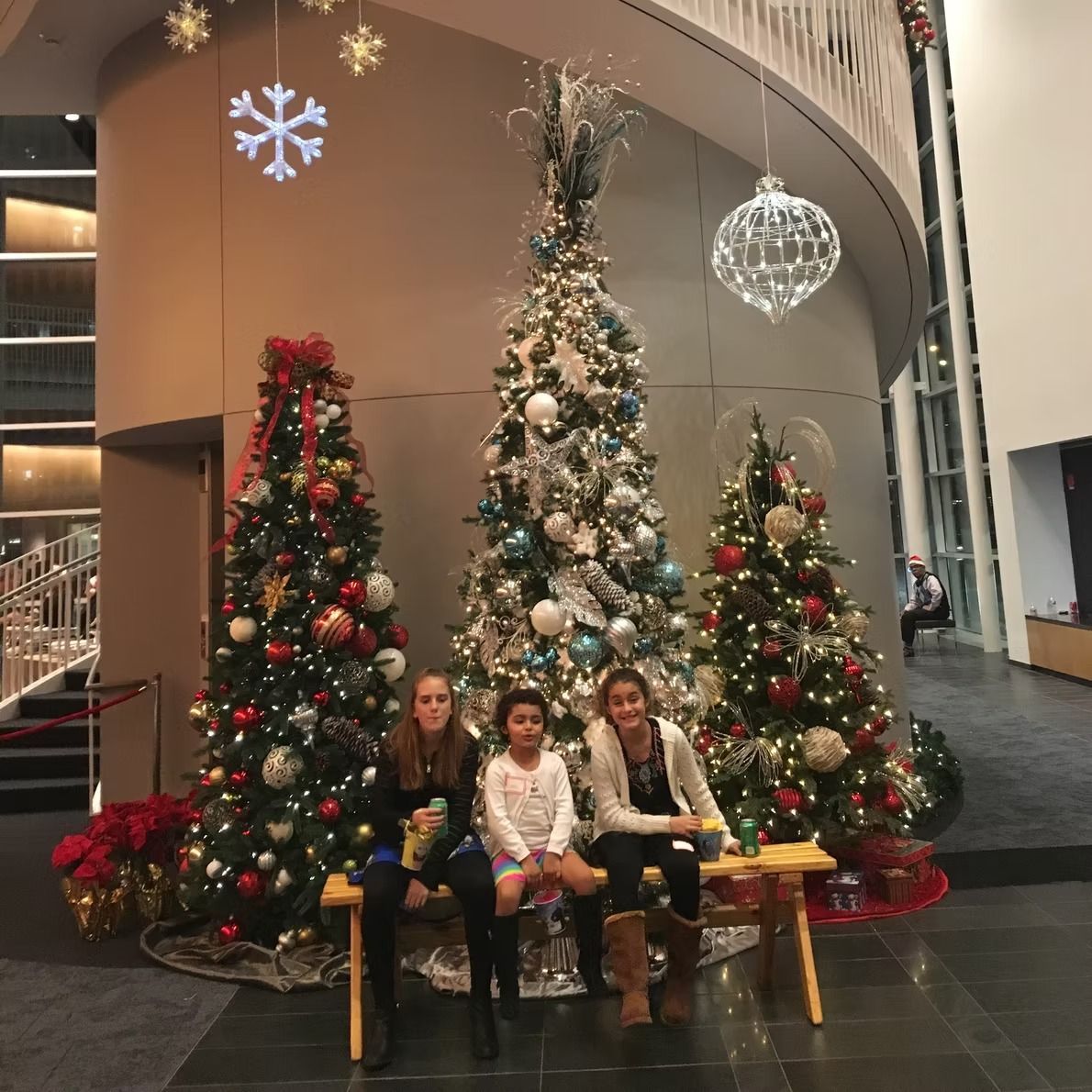Three people seated on a bench, in front of decorated Christmas trees.
