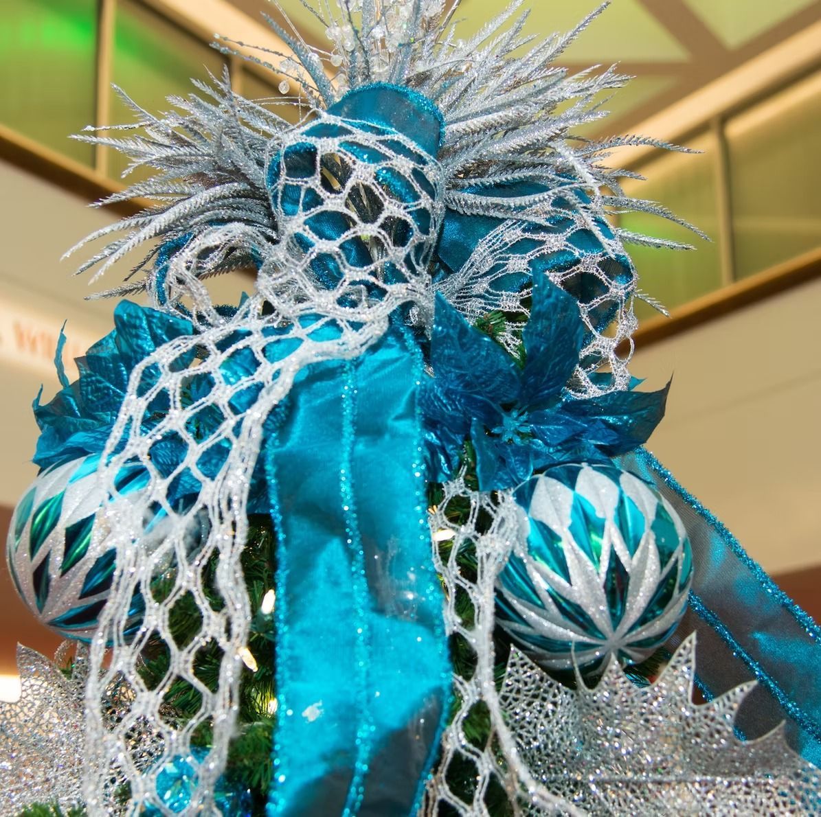 Teal and silver Christmas tree topper with ornaments and ribbon.
