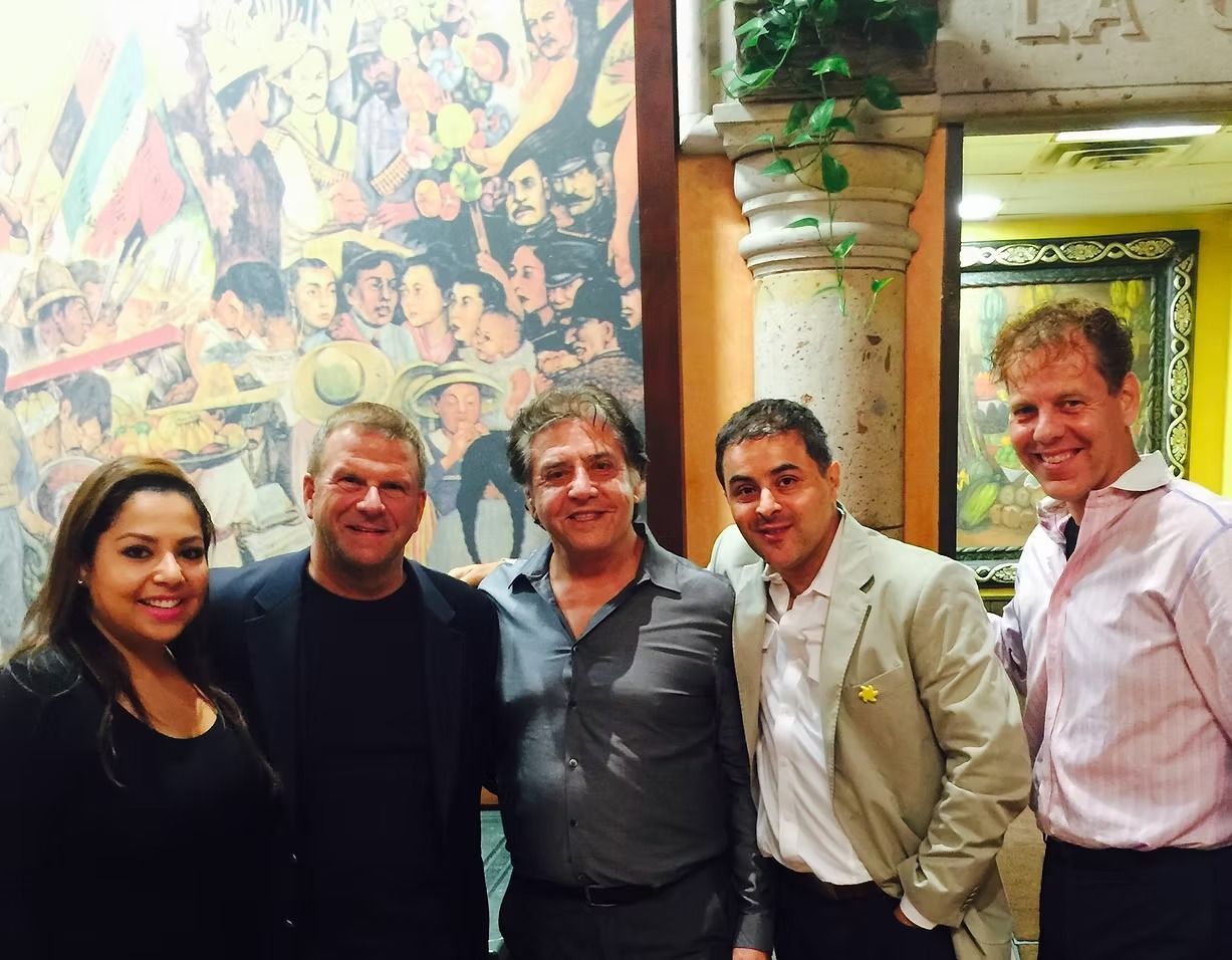 Group of five people posing in front of a mural and a column, smiling.