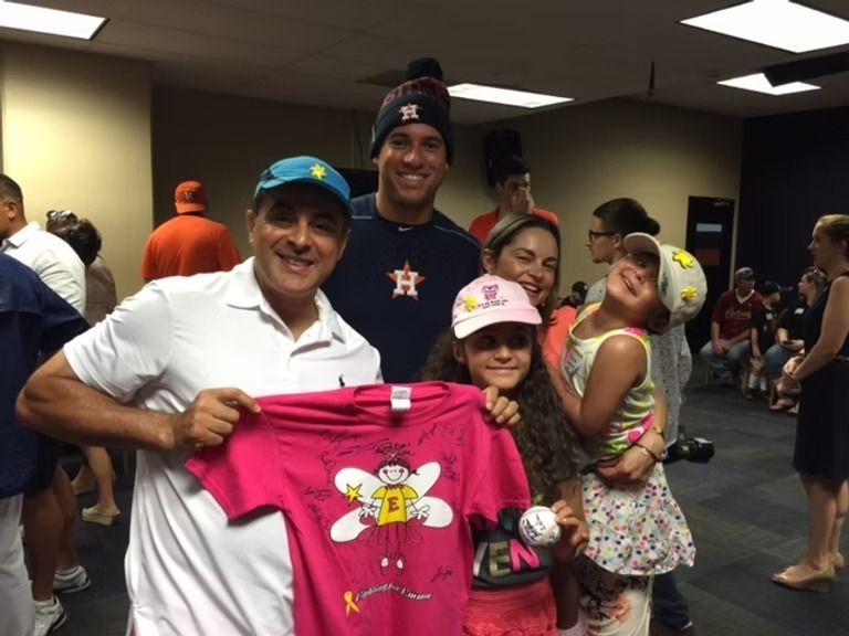 Man holding signed pink shirt, posing with baseball player and family; indoor setting.