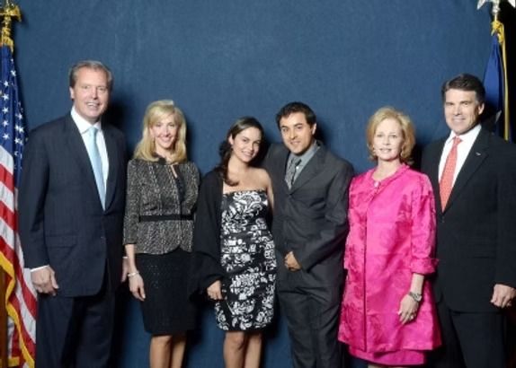 Group of six people posing for a photo against a dark blue background with flags.