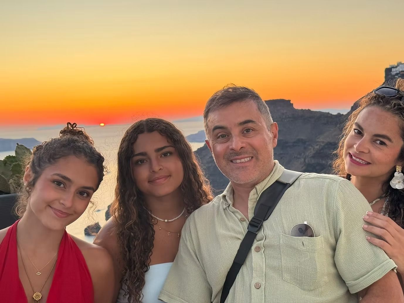 Family of four smiling, posing for photo against sunset over ocean.