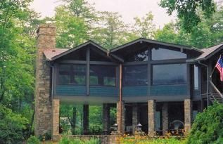 A large house with a screened in porch is surrounded by trees.