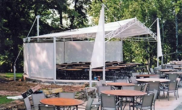 tables and chairs under a white tent in a park