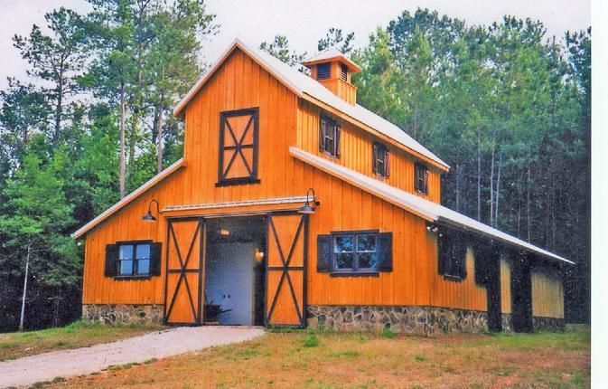 A large wooden barn with a white roof is surrounded by trees