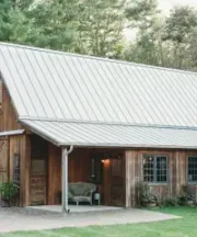 A grey house with a covered porch, white columns and railing, grey stairs, and a dark brown front door.