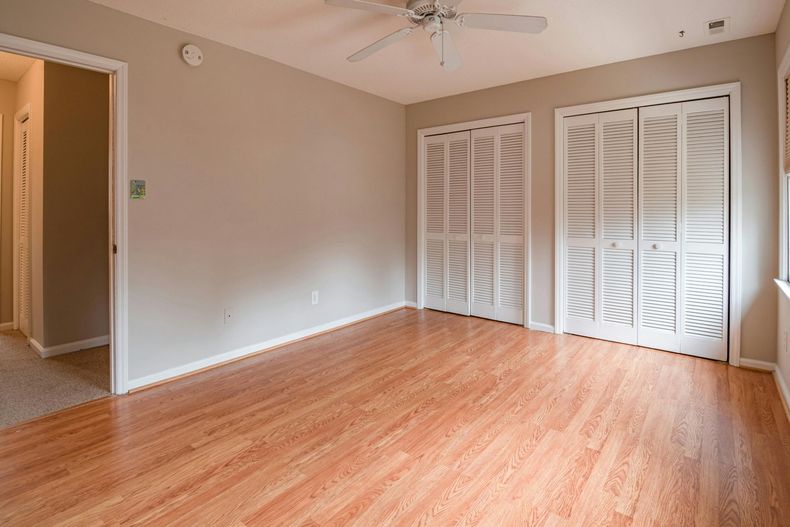 Empty bedroom with wood-look flooring, two white closet doors, and a door to another room.