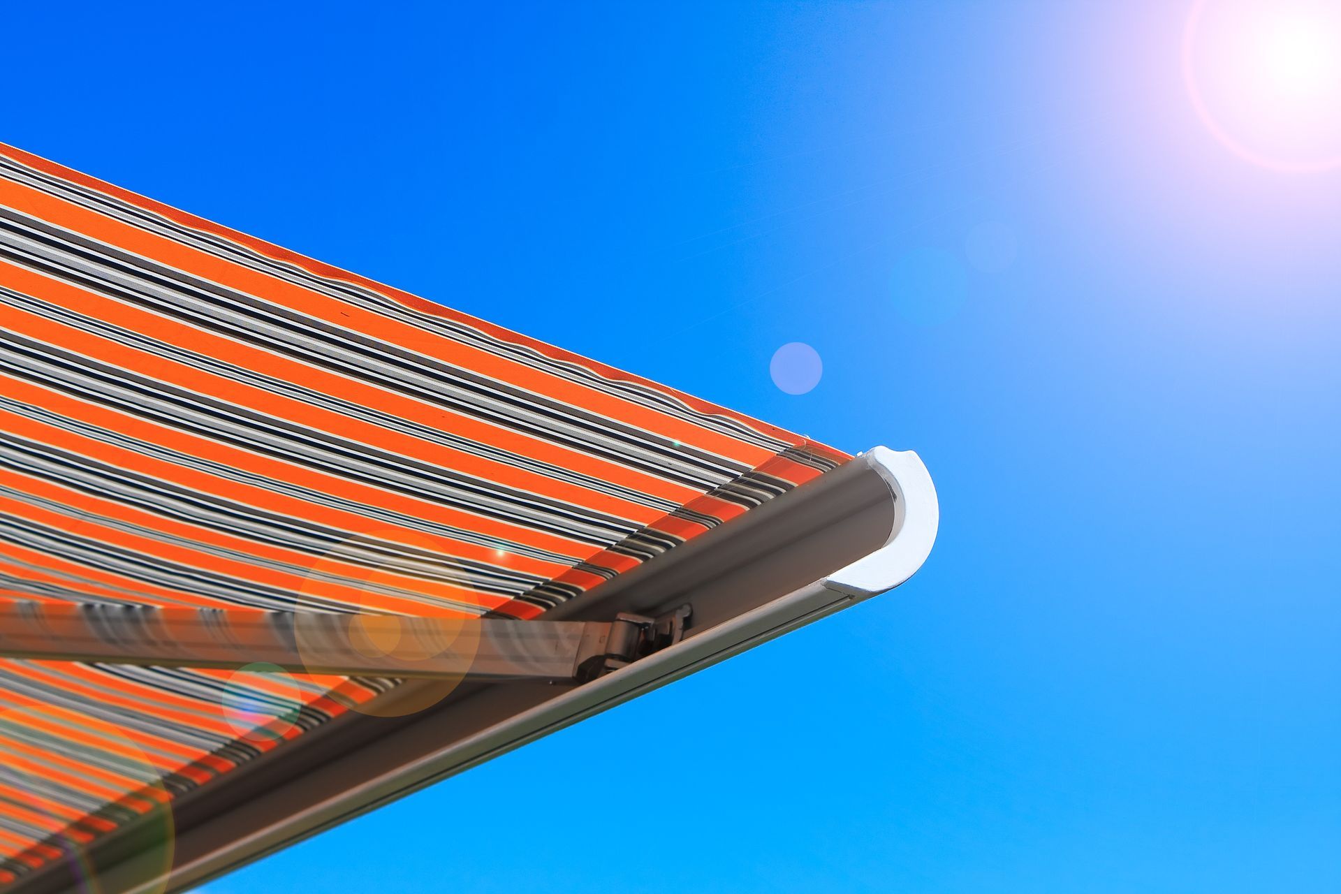 A retractable awning with a red and gray striped pattern against a clear, blue sky 