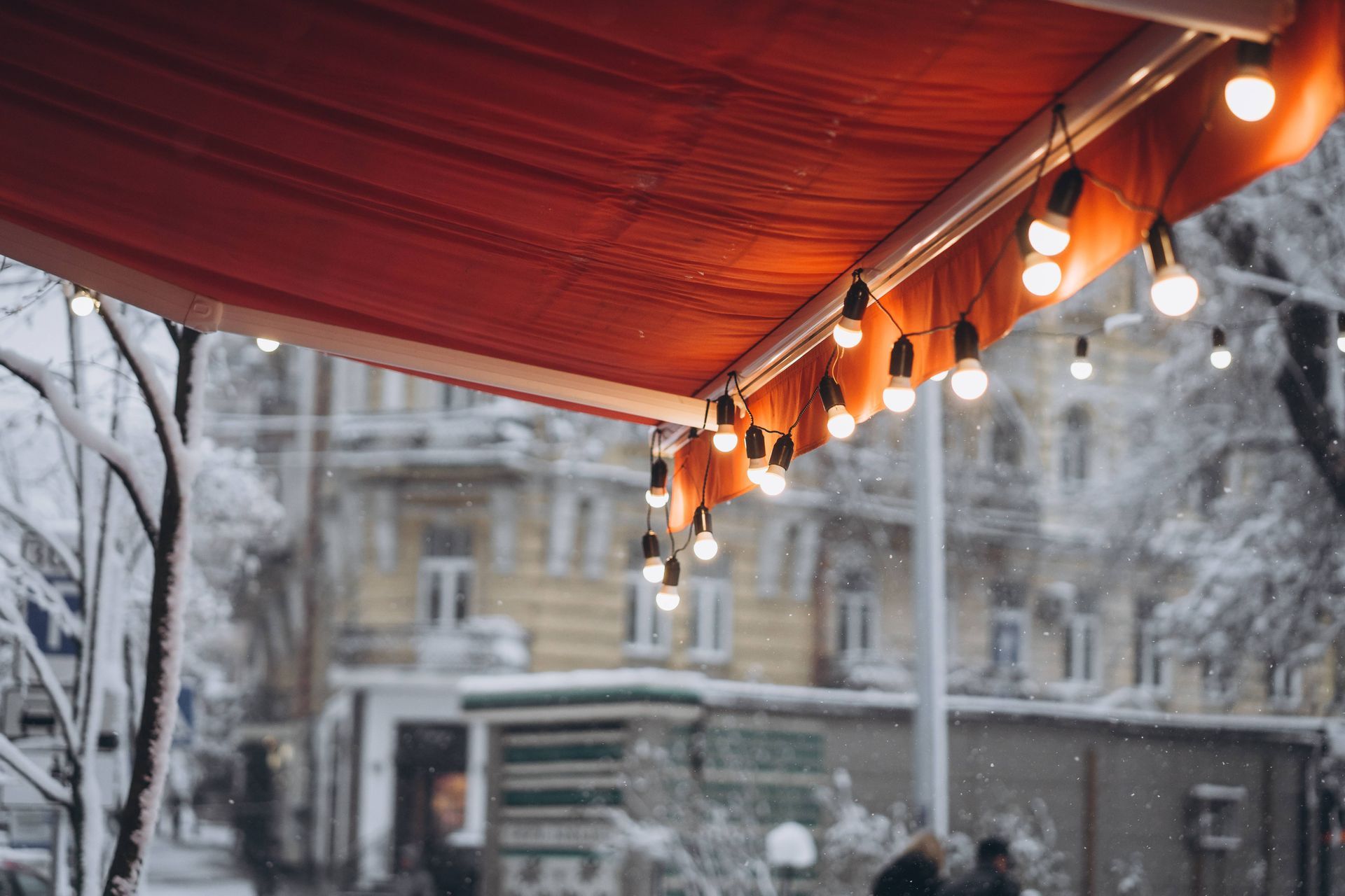 A red awning with string lights extended to the open position during a snowy winter day at The Blind