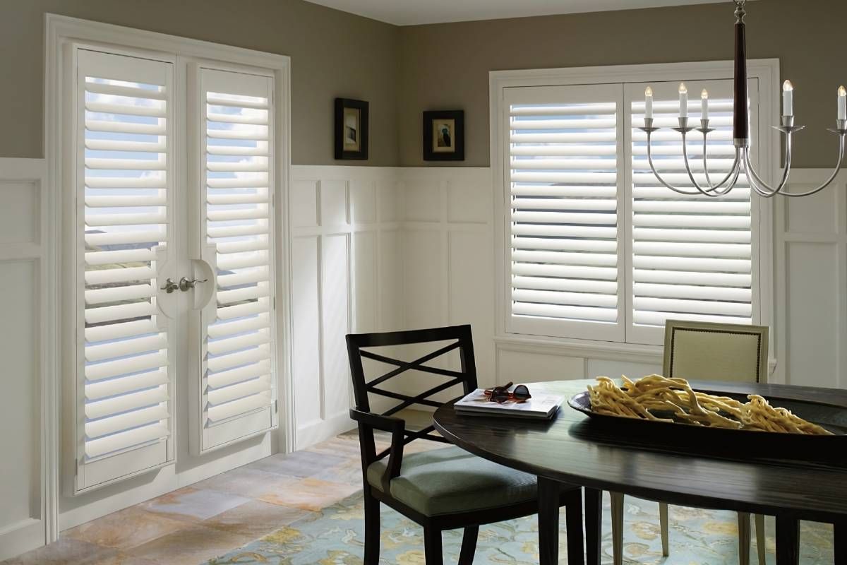 White interior shutters on French doors and a window in a formal, neutral-toned dining room