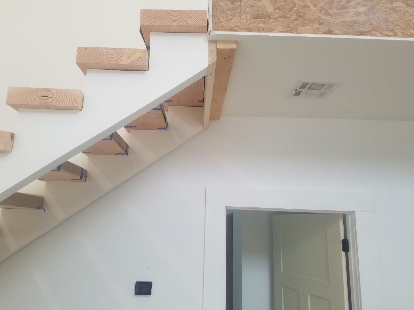 A staircase under construction with wooden treads and white risers. The setting is a bright, indoor space.