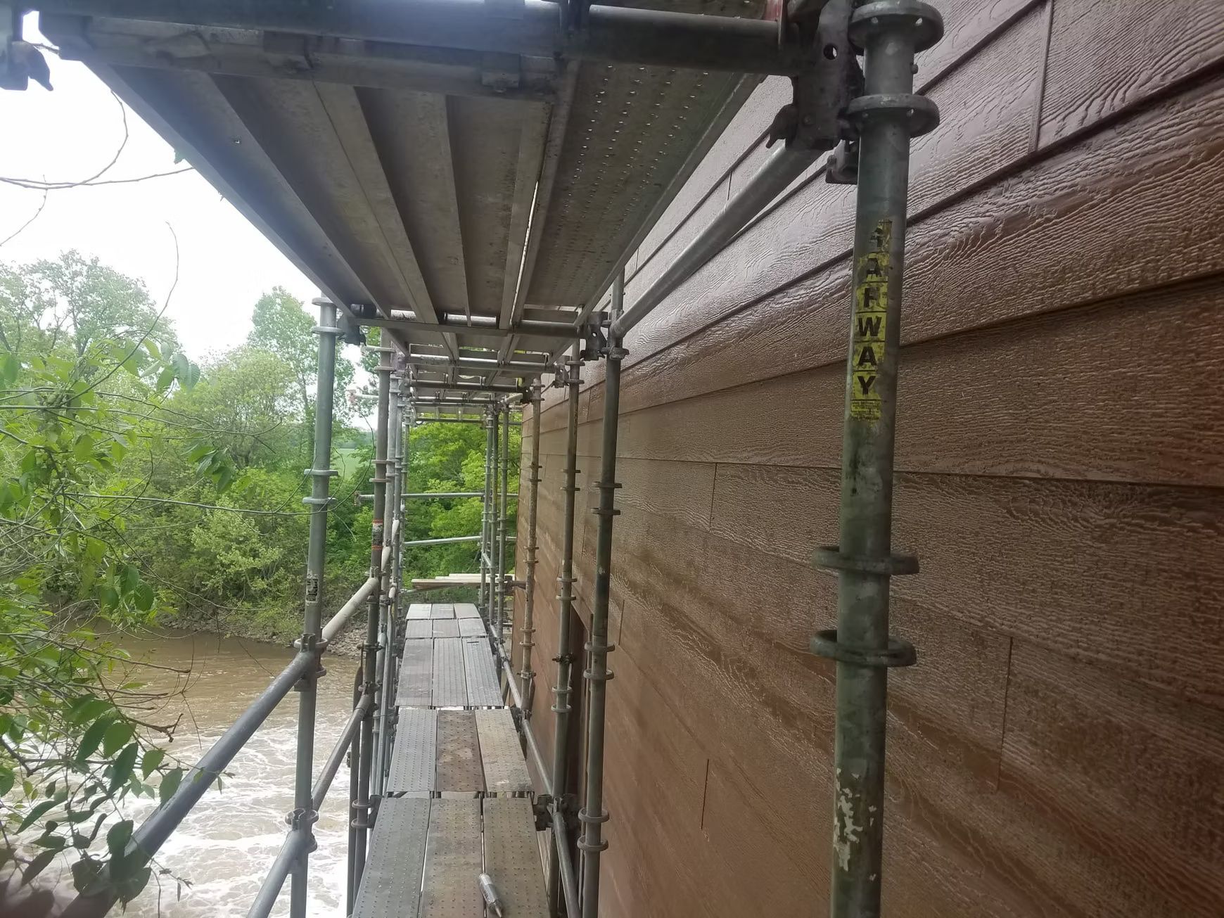 Scaffolding beside a brown-sided building, with a water-filled area visible beyond.