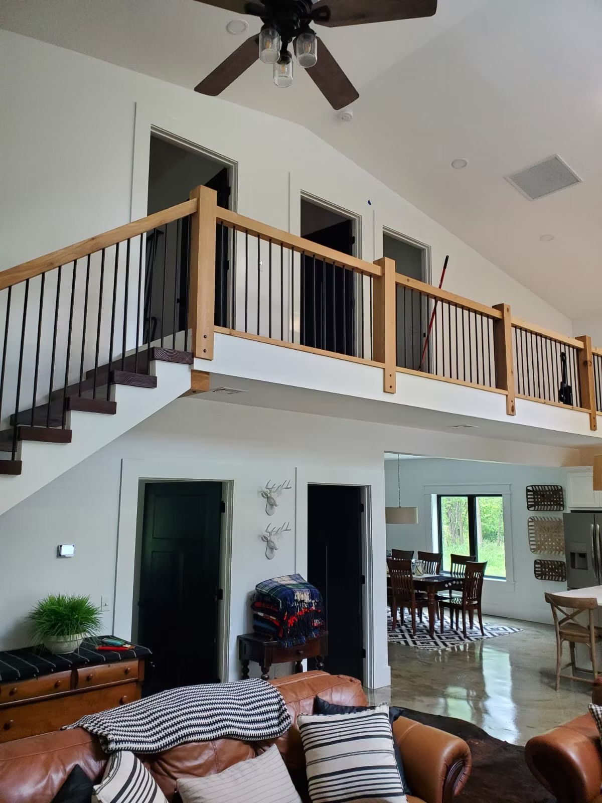 A large open living room with a loft. Features a staircase, dark doors, and a brown leather couch.
