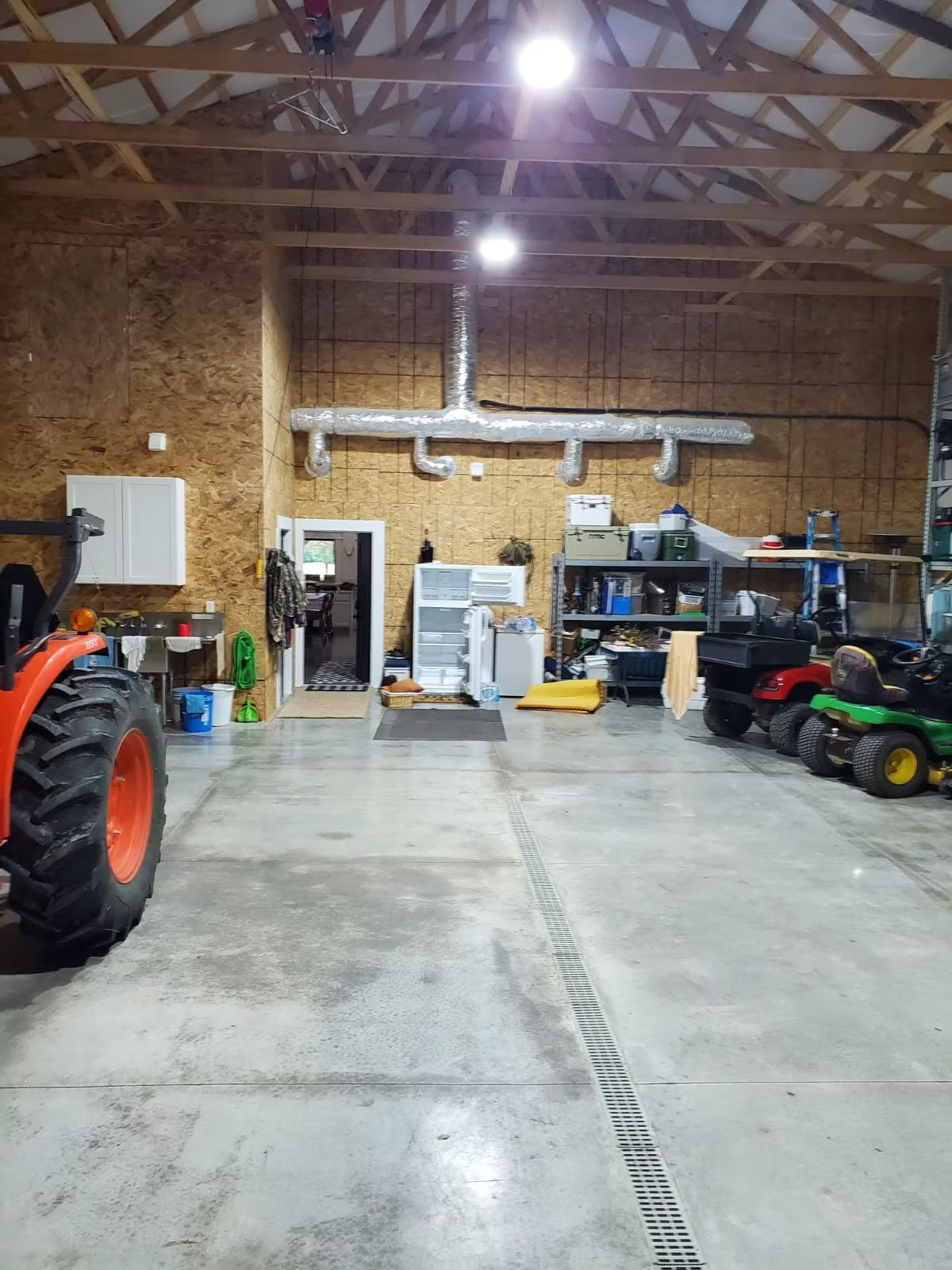 A large workshop interior with a tractor, lawnmowers, Concrete floor and exposed wooden roof structure.