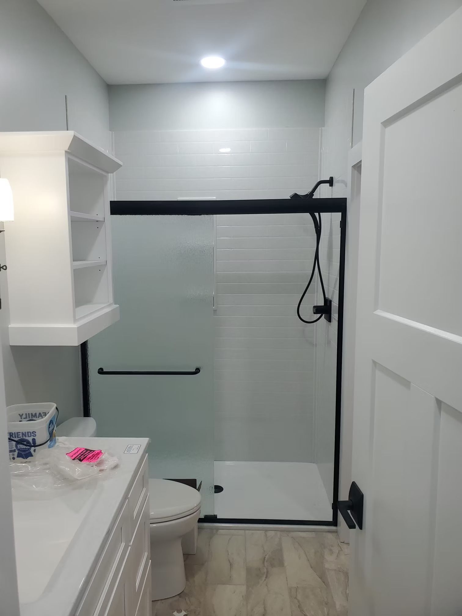 Bathroom with white walls, a shower with black trim, a white vanity, and light wood-look flooring.