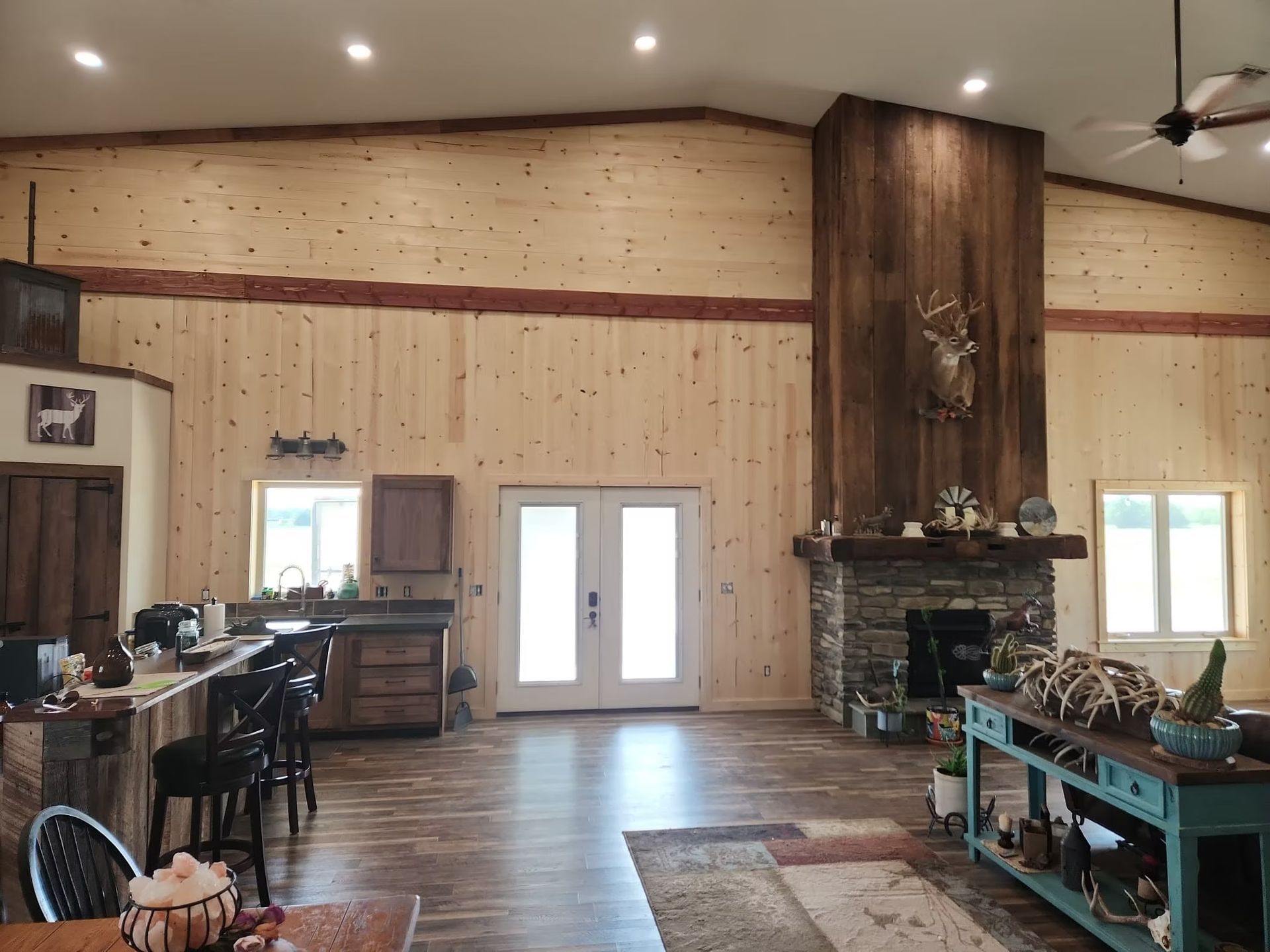 Interior view of a rustic living space with wood paneling and a fireplace. A deer head hangs above the mantle.