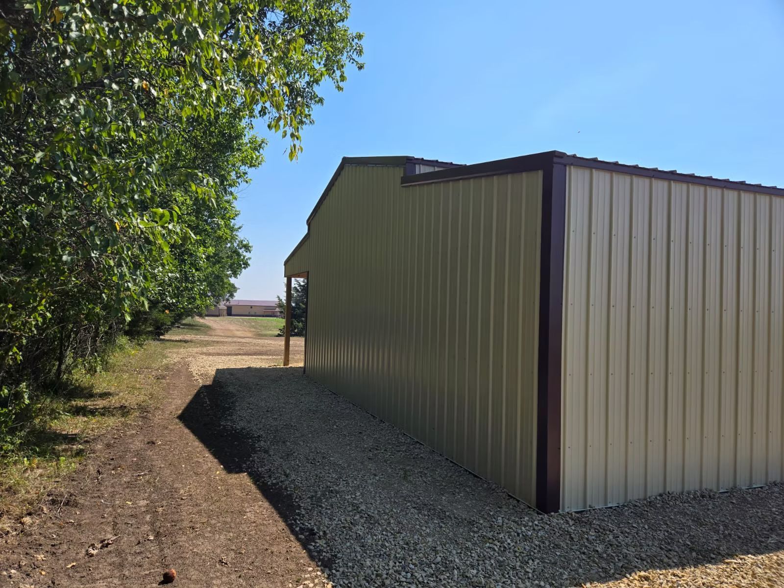 Black cabin with two windows and metal roof on a grassy lot, with a trailer in the background. Trees are in the distance.