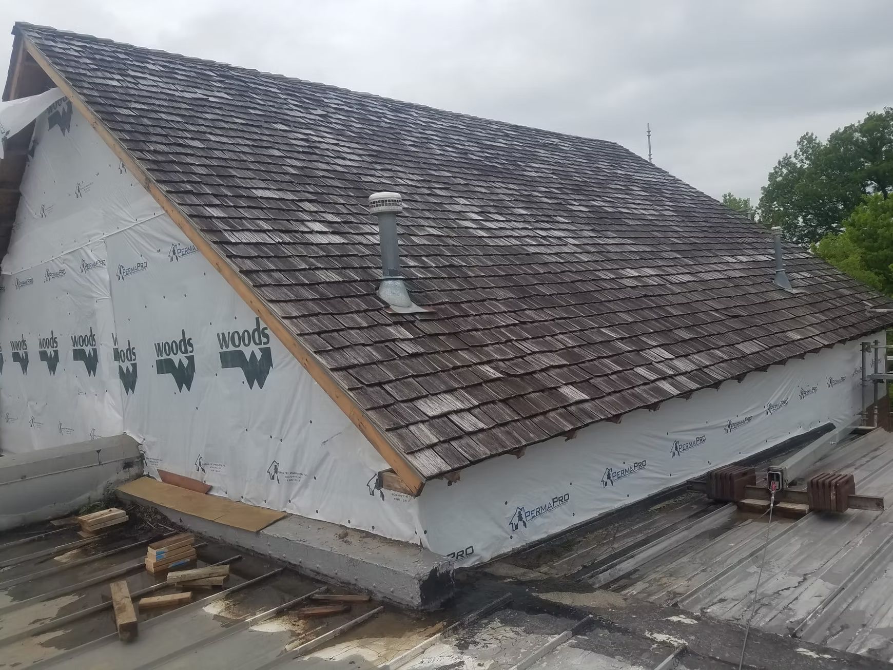 A partially constructed building with a cedar shake roof, white siding, and waterproof sheathing, sitting on a metal roof.