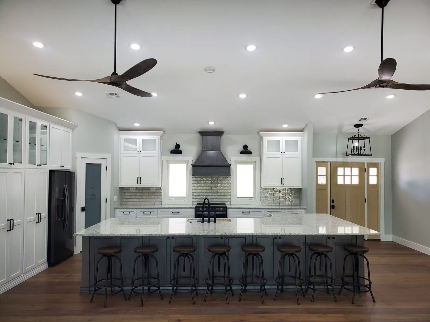 Spacious kitchen with a large , grey cabinets, and a granite countertop. Includes a light wood door and two ceiling fans.