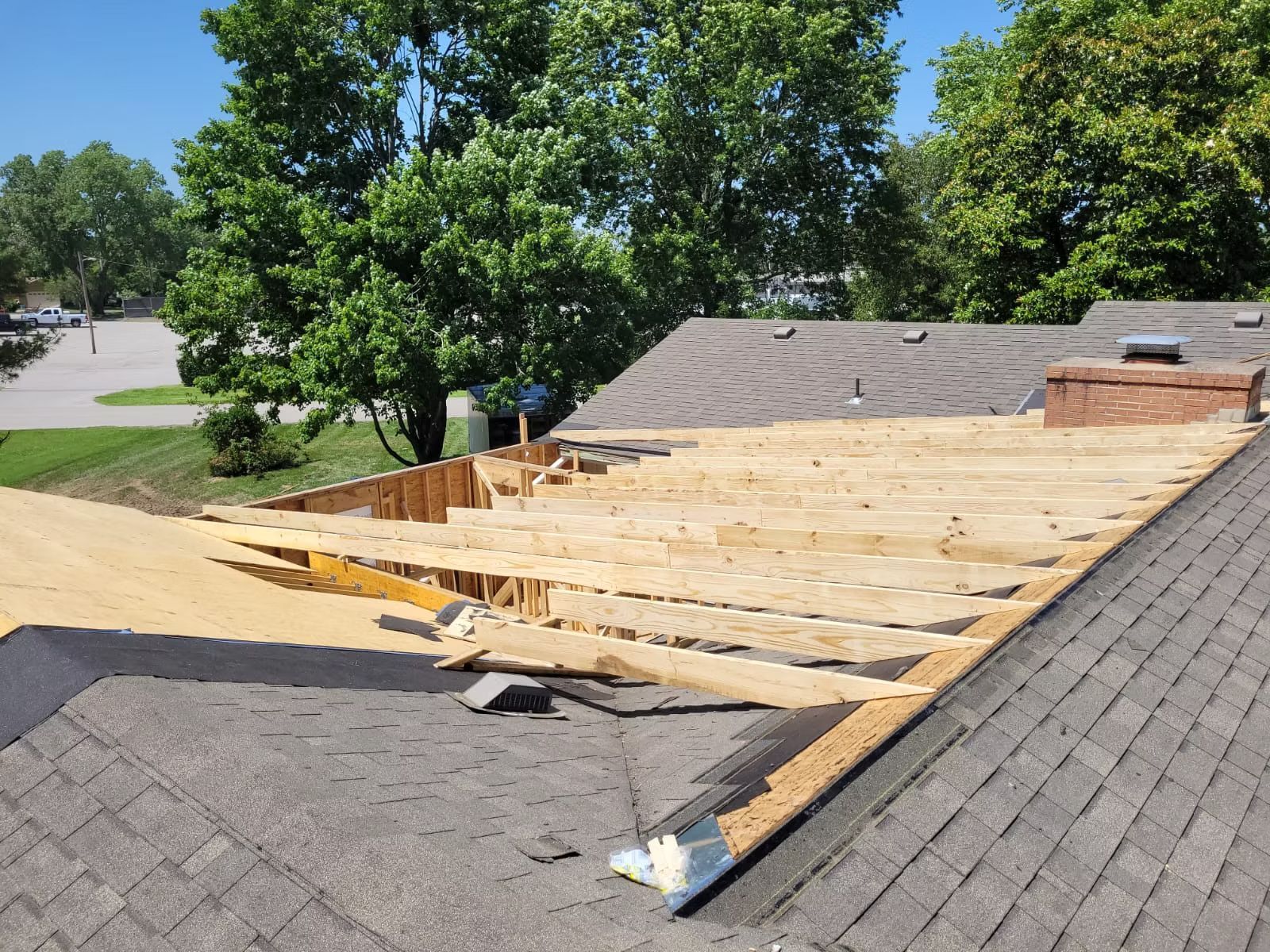 Roof of a house partially dismantled, revealing wooden supports, with dark grey shingles remaining on the right.