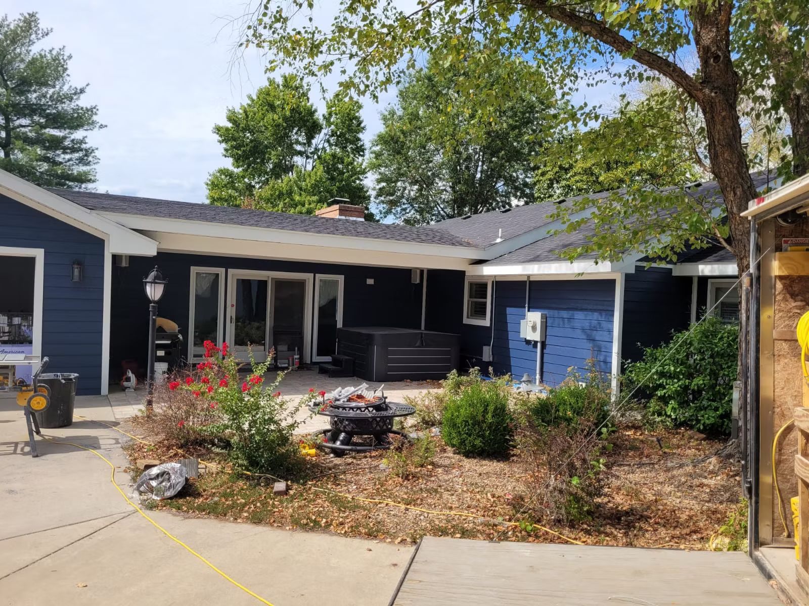 Tan metal building with a brown wooden porch, featuring seating and hanging plants. Gravel driveway.