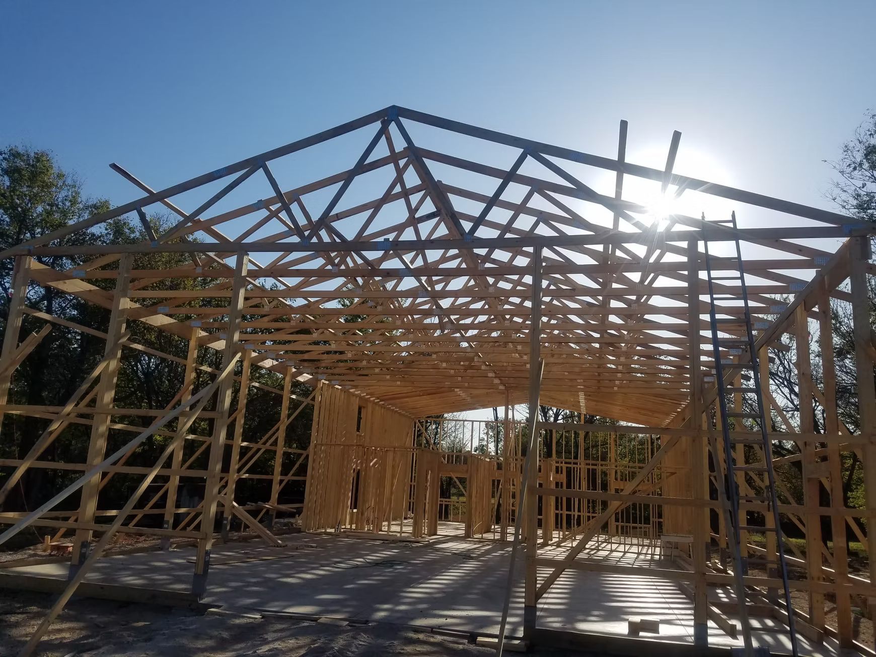 Wooden structure of a building under construction, with the sun shining brightly through the roof beams.
