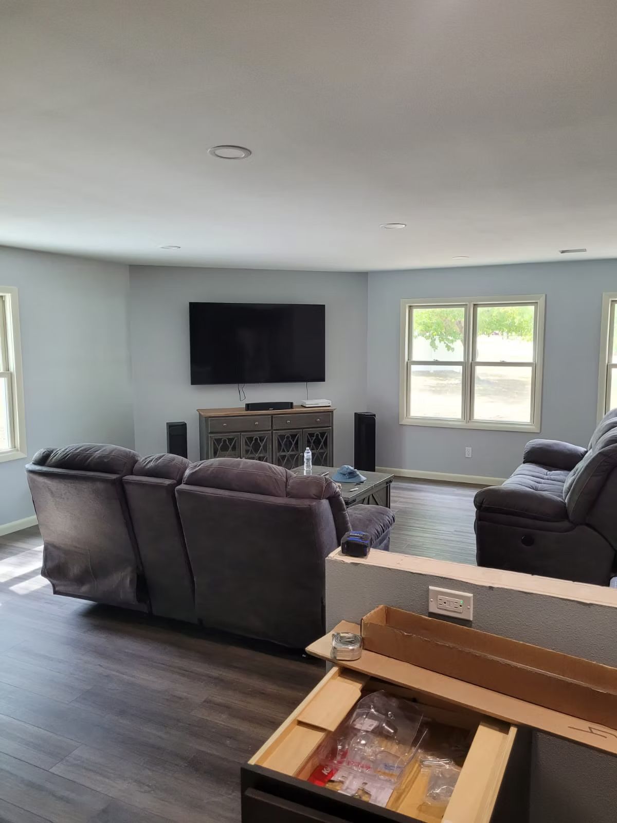 A living room with a large TV, grey sectional sofa, and hardwood floors. The walls are painted light blue.