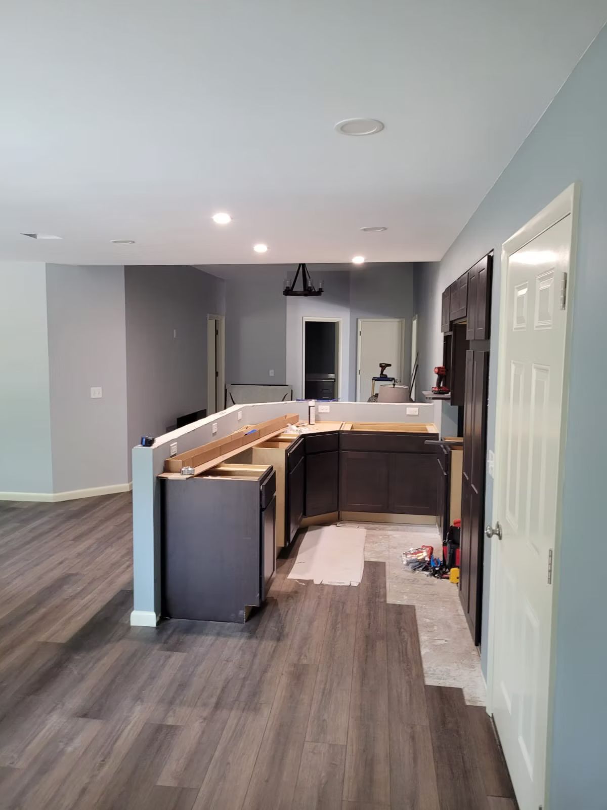 Kitchen under construction; dark cabinets, countertop, and flooring installed. Grey walls and a white door are also visible.