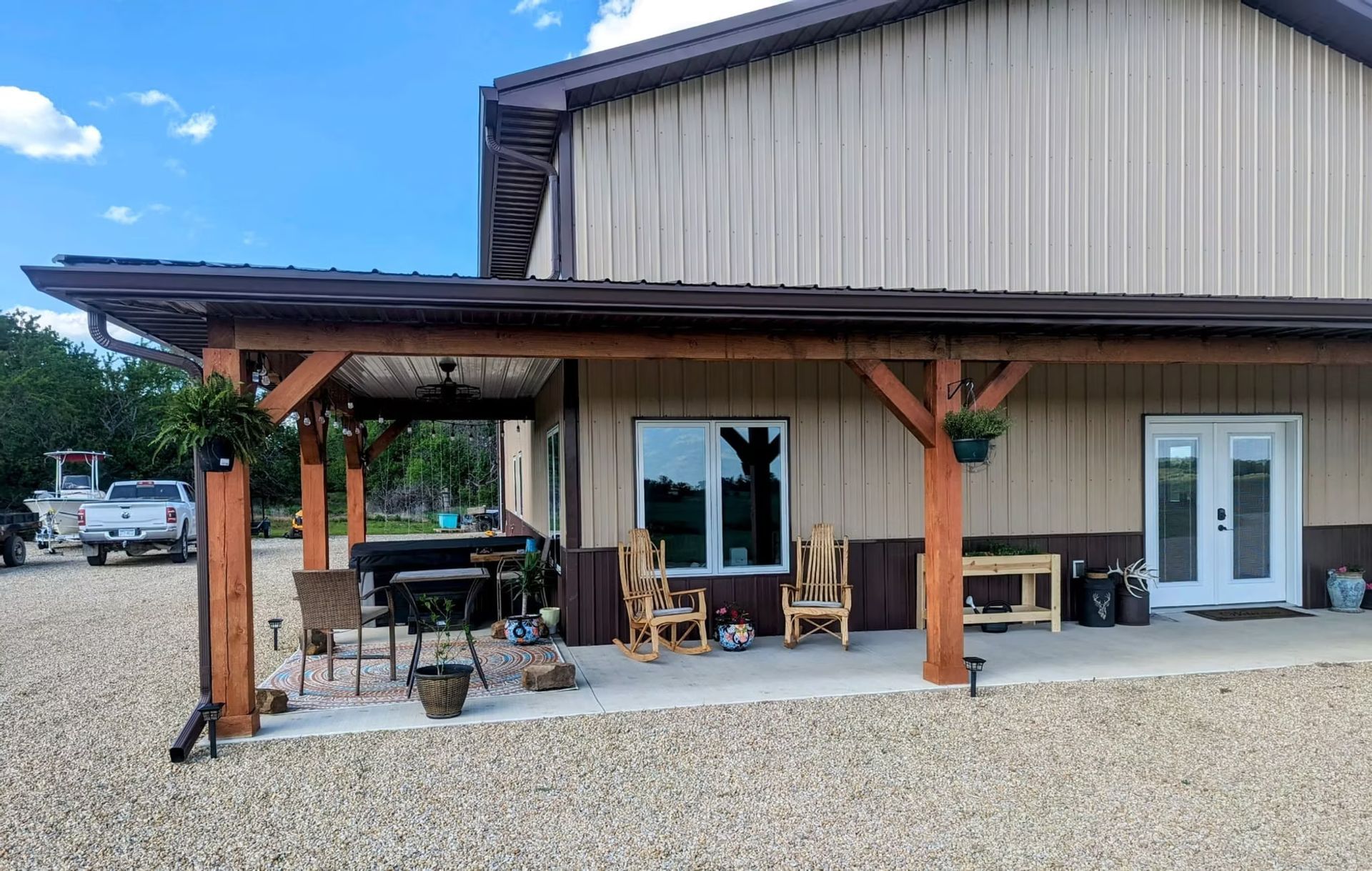 A tan building with a brown awning and patio. The patio has seatgravel driveway.