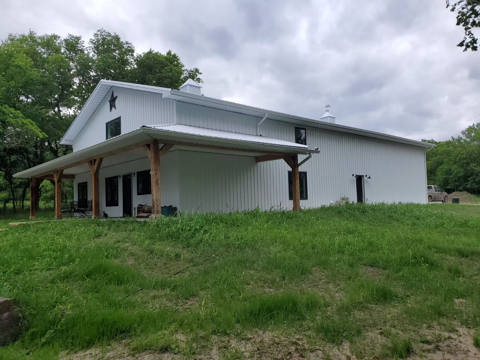 White barn-style house with a porch and a metal roof, set on a grassy hill against a cloudy sky.