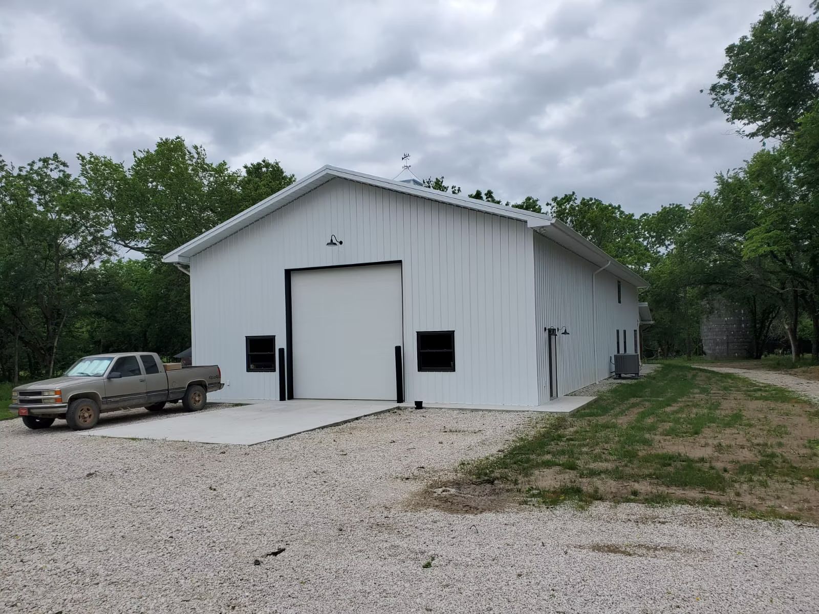A white metal building with a large overhead door and a pickup truck parked on gravel.
