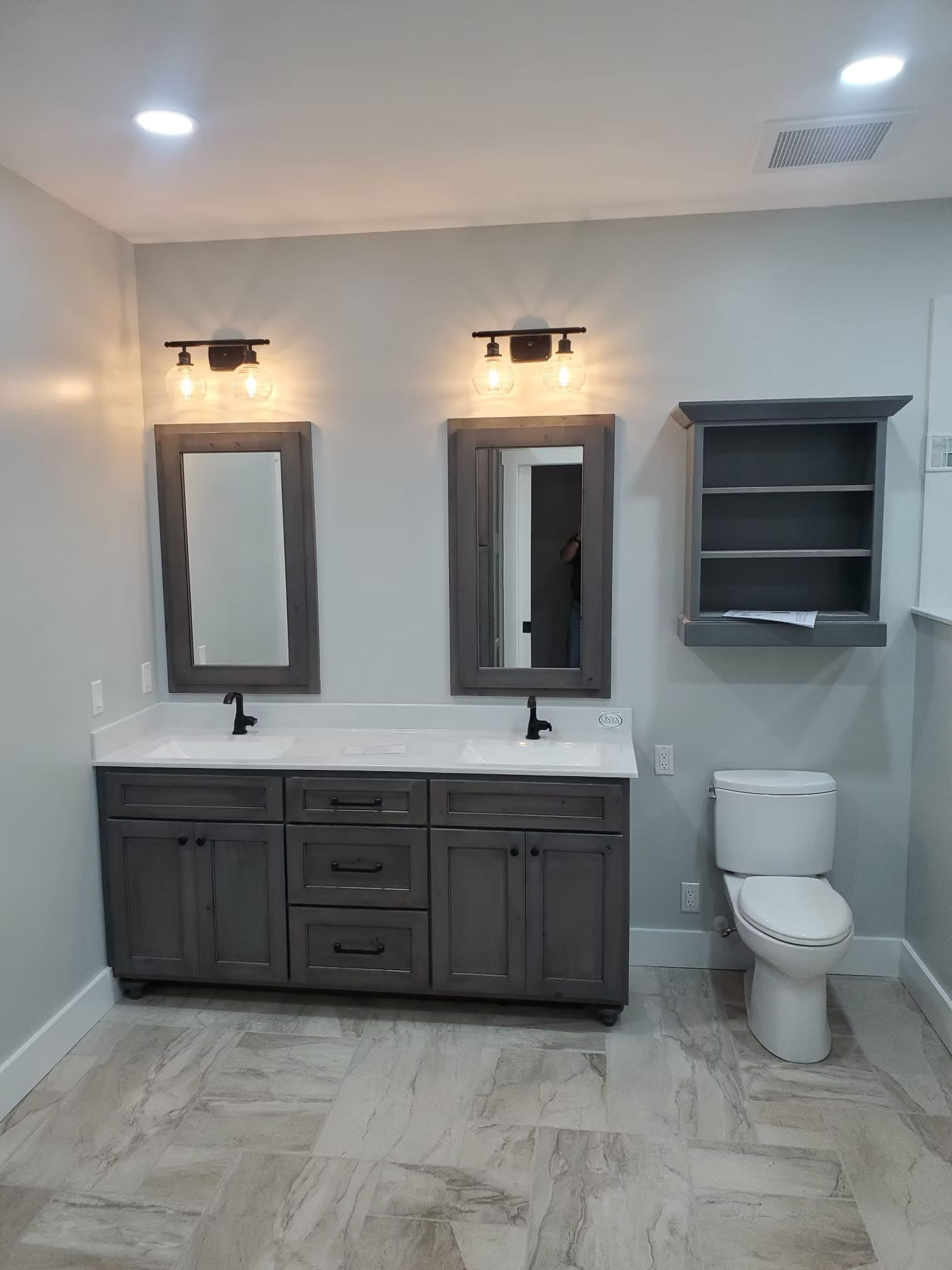 Bathroom with gray double vanity, mirrors, and a matching wall cabinet; white toilet and light gray walls.