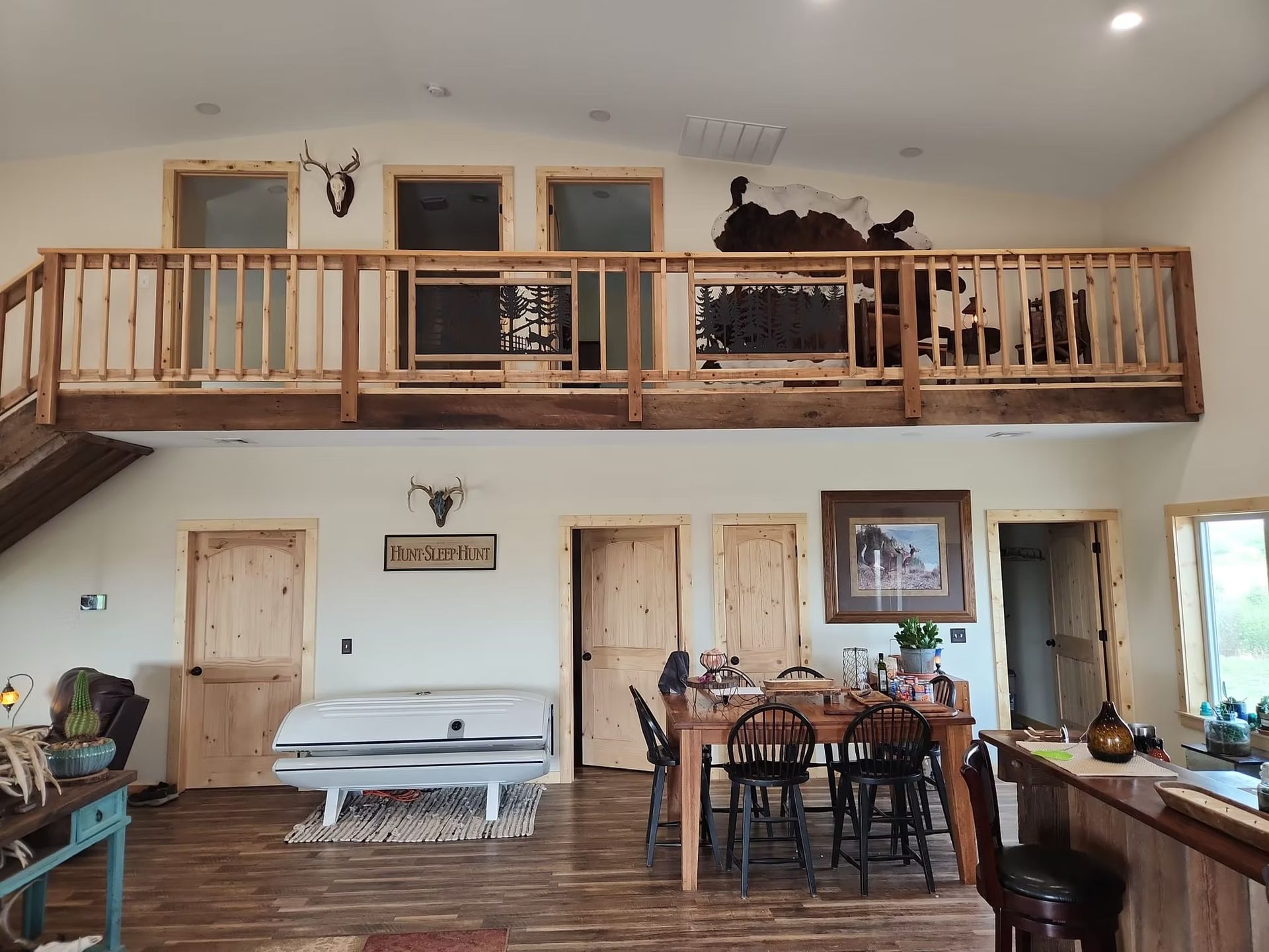 Open-concept living area with a loft. Features a dining table, cowhide rugs, and rustic wooden elements.