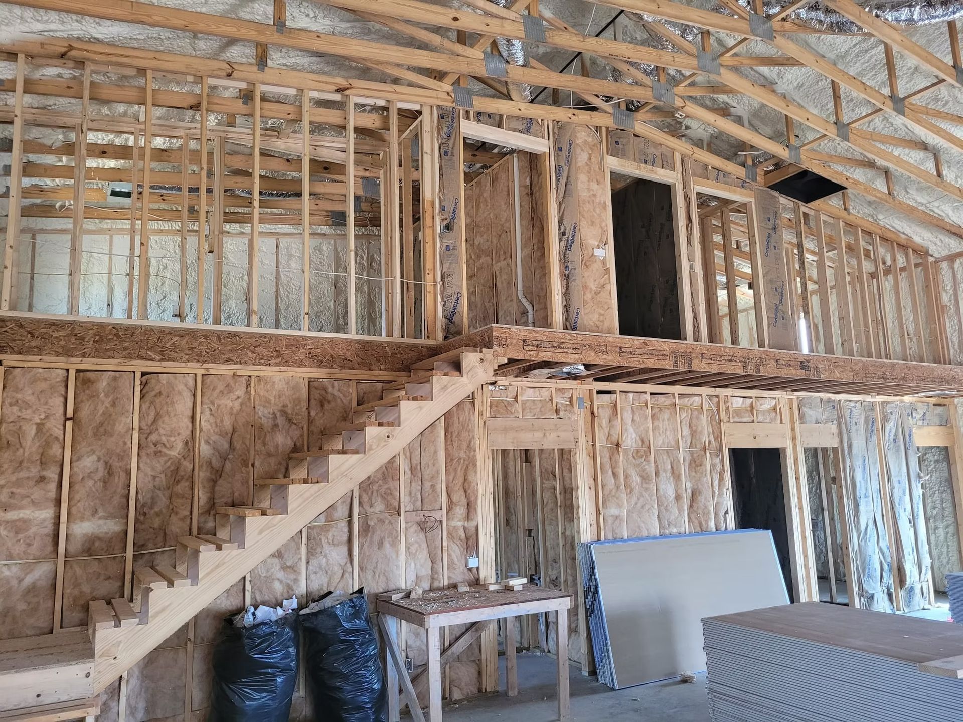 Interior of a building under construction, showing wooden framing, a staircase, and a loft area. Insulation is the walls.