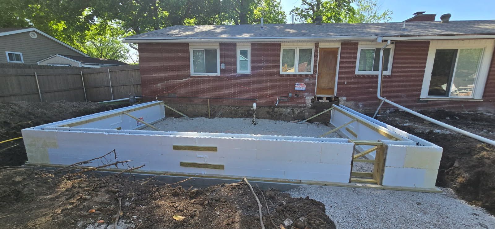 Backyard construction of a white concrete foundation beside a red brick house