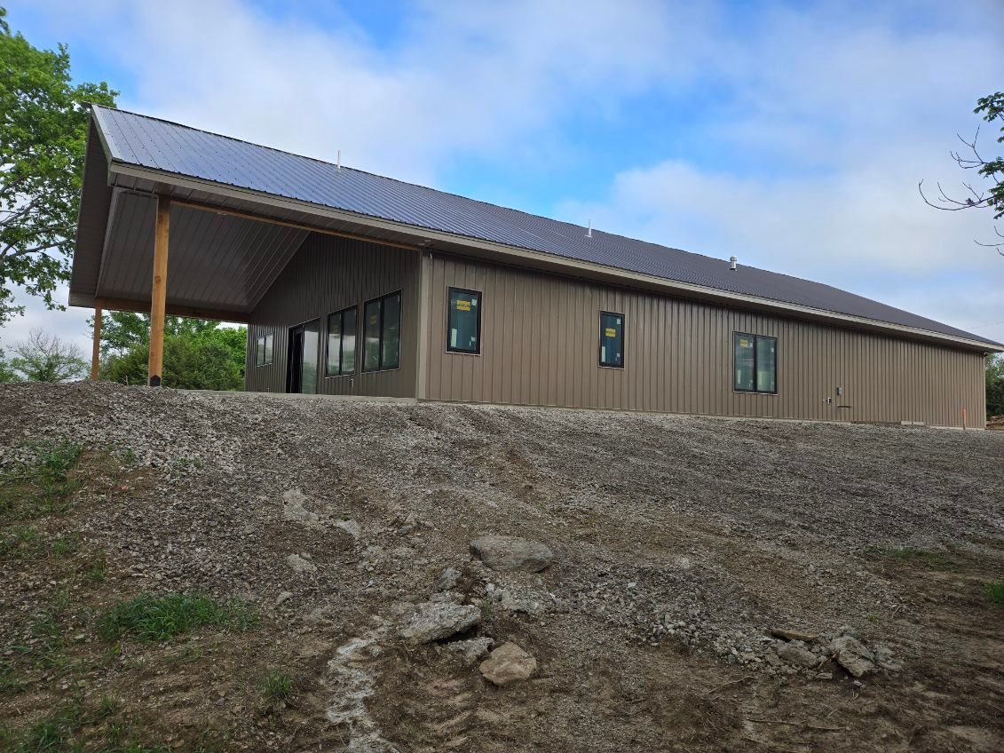 Long, tan building with a metal roof on a dirt hillside under a partly cloudy sky