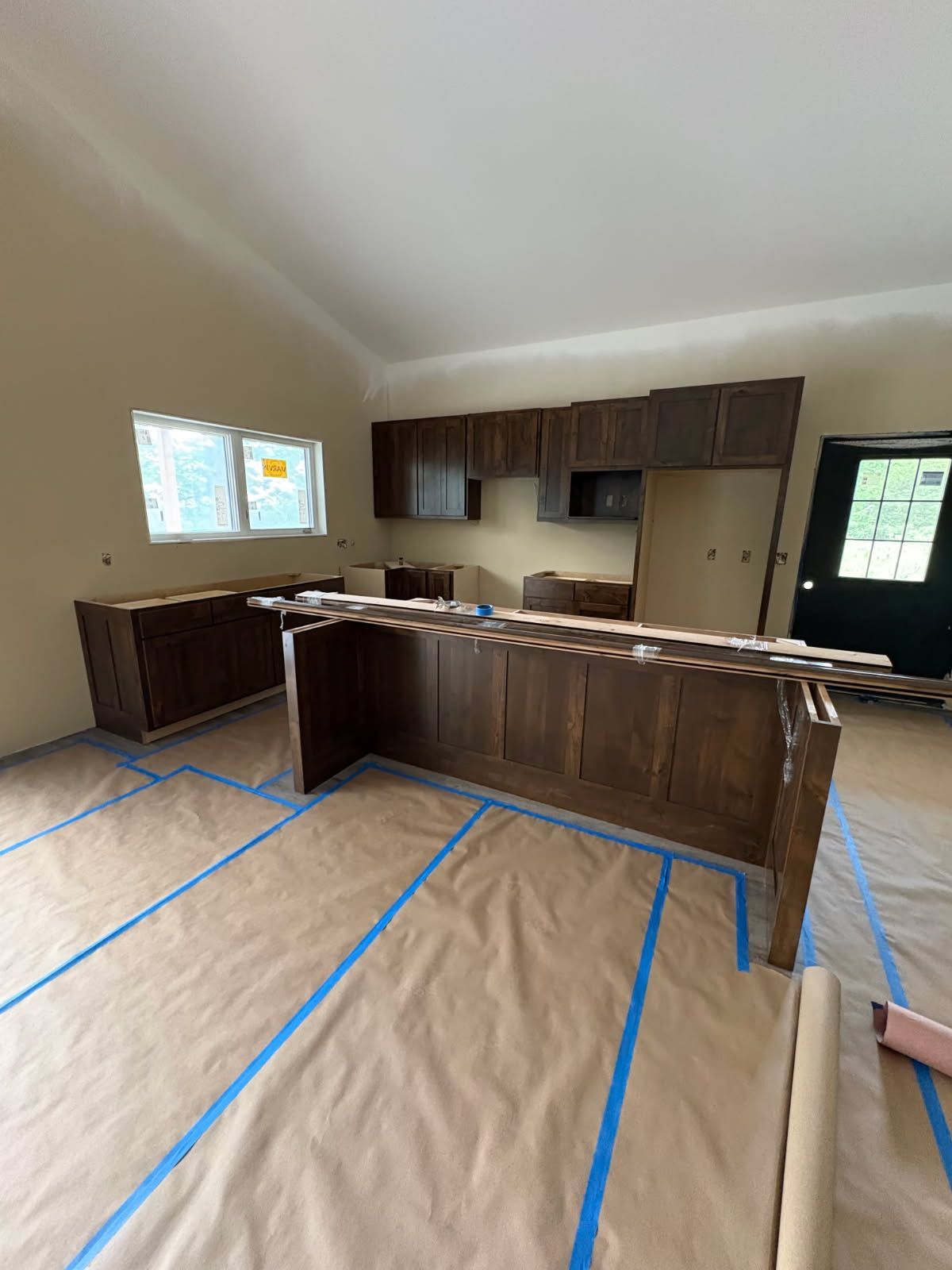 Unfinished kitchen with dark cabinets, island, taped floor protection, and window light