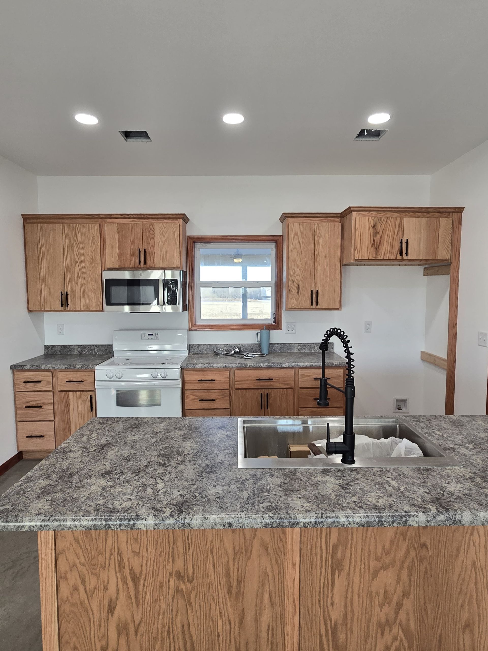 Construction site with a cono a light gray house. Rebar sticks up from the concrete. A small excavator is visible.